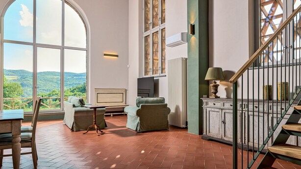 Een ruime kamer met een groot rondboogvenster, met uitzicht op het platteland.