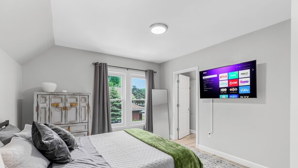 A bedroom with a bed, a dresser, a TV mounted on the wall, and a window with curtains. - Cozy & Quiet Studio Flat in Historic Mount Clemens (Mount Clemens)