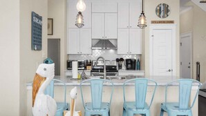 Una cocina con armarios blancos, una isla central con sillas azules y lámparas colgantes.