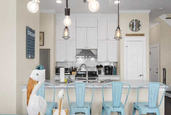 A kitchen with white cabinets, a central island with blue chairs, and hanging light fixtures. - Relaxing 4BR Beachside Home with Hot Tub | Pet Friendly (Galveston)