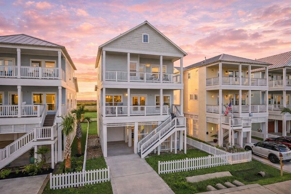 A beachfront hotel with multiple balconies, a central staircase, and a flag. - Relaxing 4BR Beachside Home with Hot Tub | Pet Friendly (Galveston)