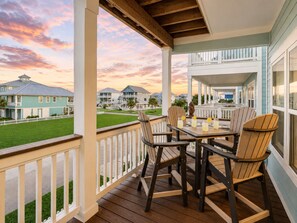 A covered outdoor seating area with a view of a residential neighborhood during sunset. - Relaxing 4BR Beachside Home with Hot Tub | Pet Friendly (Galveston)