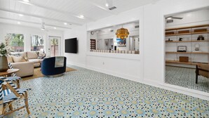 Una sala de estar moderna con piso estampado, un sofá, un sillón azul y un televisor montado en la pared.