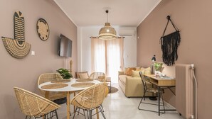 A modern living room with a dining area, featuring wicker furniture, a large pendant light, and a television on the wall. - Boho Pennie Home by CloudKeys (Athens)