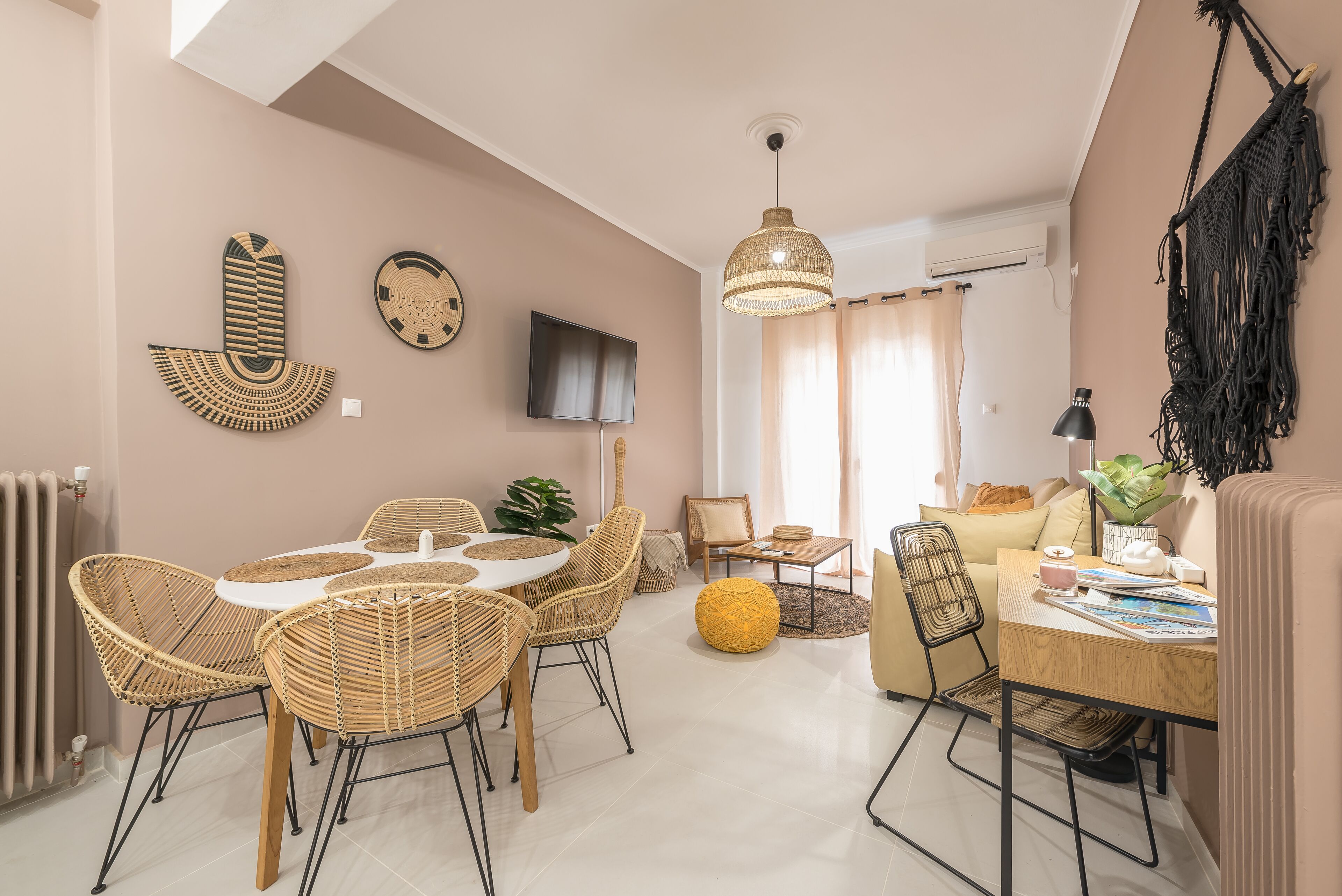 Un salon moderne avec un coin repas, comprenant des meubles en osier, un grand luminaire suspendu et un téléviseur à écran plat fixé au mur.