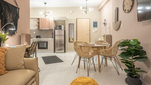A modern kitchen with stainless steel appliances, a dining area with wicker chairs, and a cozy seating area with a sofa and a potted plant. - Boho Pennie Home by CloudKeys (Athens)