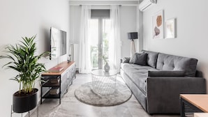 Ett modernt vardagsrum med en grå soffa, ett runt soffbord, en krukväxt och en tv som står på ett tv-bord.