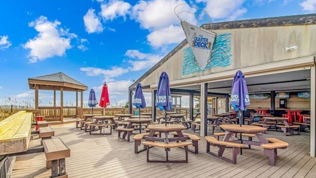 An outdoor deck with wooden picnic tables and umbrellas, a wooden gazebo, and a building with a mural. - Updated Ocean View 2BR|2BA Condo (Myrtle Beach)