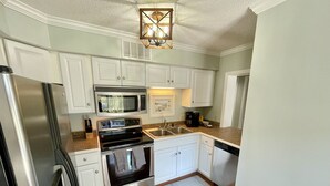A kitchen with white cabinets, stainless steel appliances, a wooden countertop, and a hanging light fixture. - Updated Ocean View 2BR|2BA Condo (Myrtle Beach)