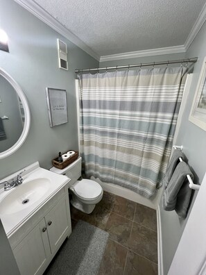 Een badkamer met een wit wastafelmeubel, toilet en een douchegordijn met strepen.