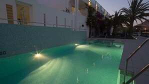 A swimming pool with steps leading down to it, surrounded by a white building with balconies and palm trees. - Hostal Las Gaviotas del Cabo (Nijar)
