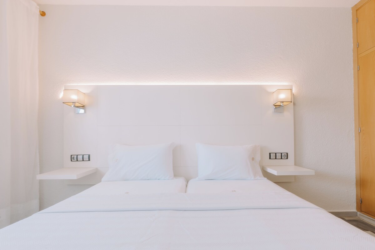 Una habitación de hotel con una cama grande, dos mesitas de noche e iluminación en la pared.