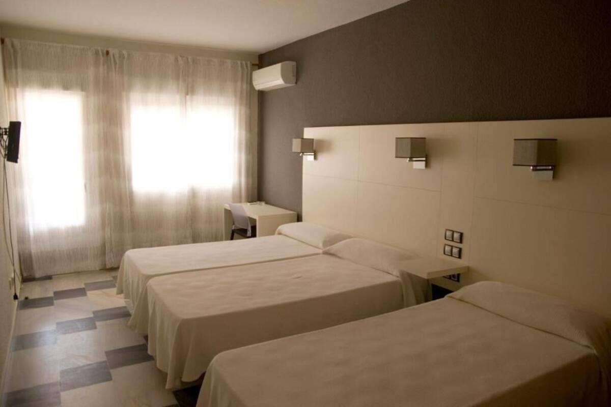 A hotel room with three beds, a desk, and a chair.