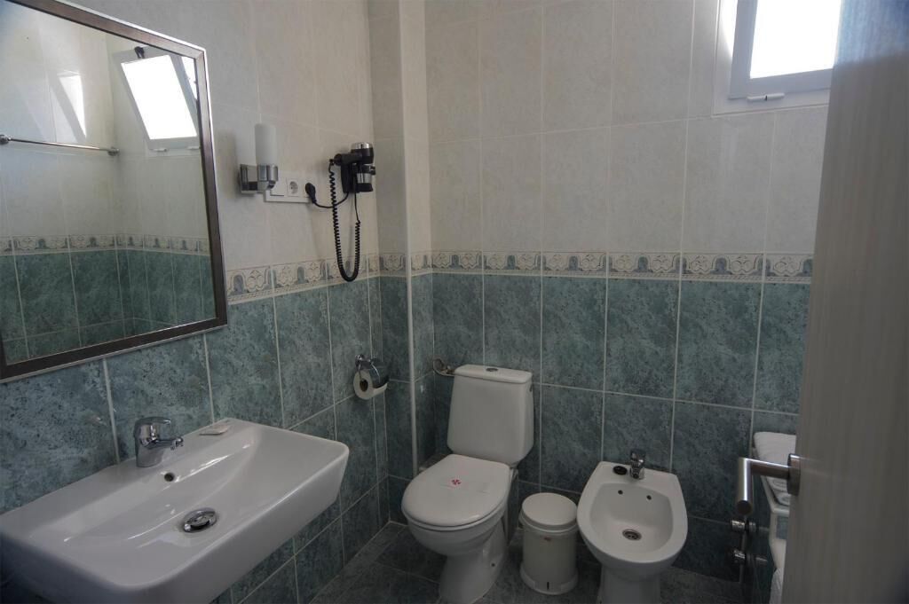 A bathroom with a sink, toilet, bidet, and a mirror.