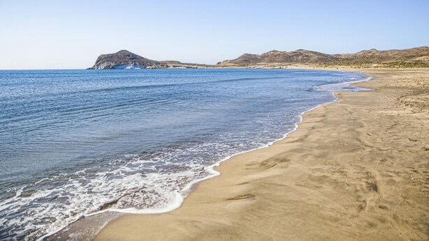 A beach with clear blue water, sandy shore, and rocky hills in the background. - Hostal Las Gaviotas del Cabo (Nijar)
