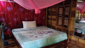 Una cama de madera con una colcha estampada, un ventilador de pie y un espejo en la pared.