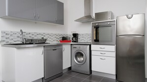 A modern kitchen with stainless steel appliances, grey cabinets, and a tiled backsplash. - Apartment 60 M2 with 2 Bedrooms and 2 shower rooms Sea View 300 M from the sea (Sainte-Maxime)