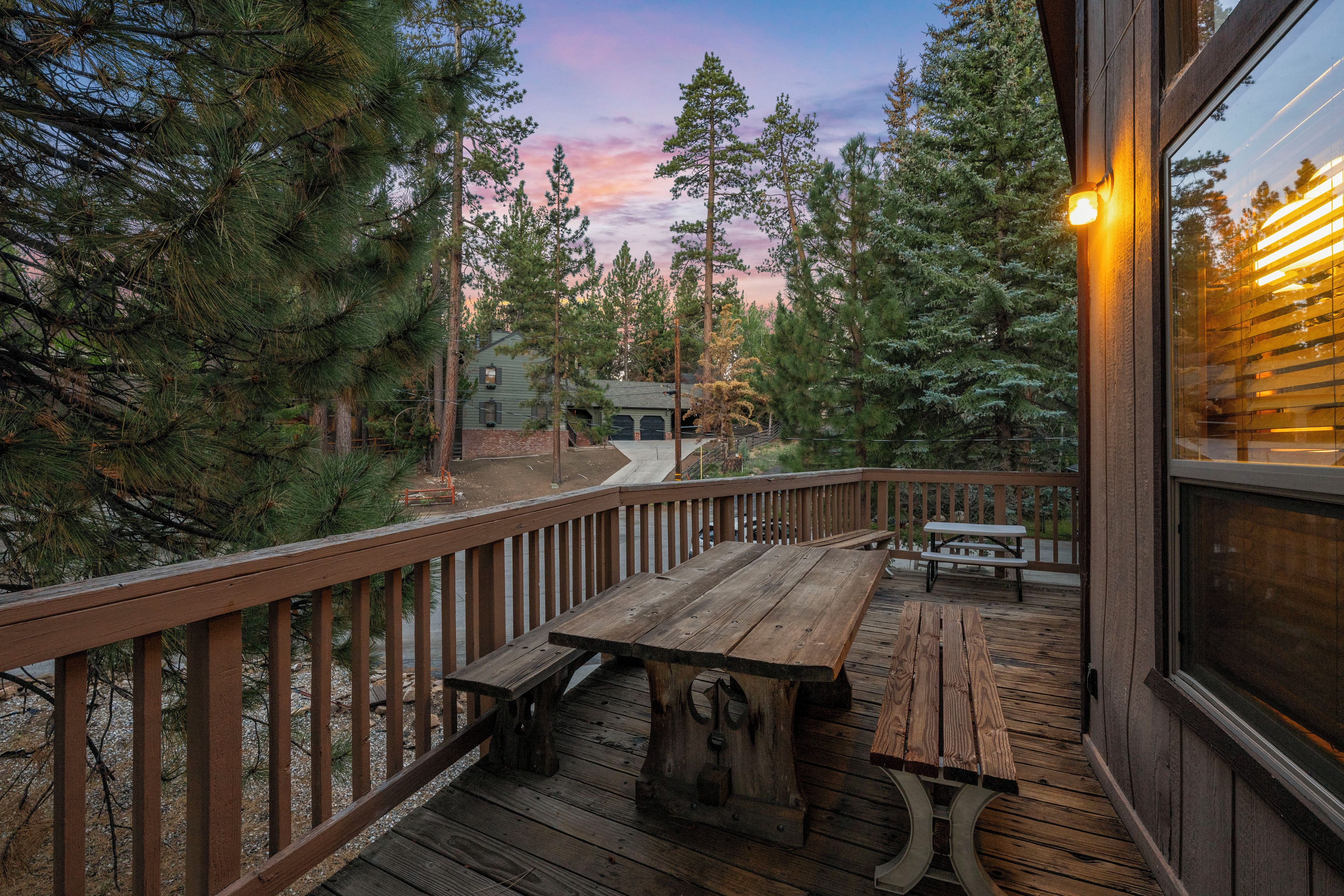 A wooden deck with picnic tables, surrounded by trees and a building with a green roof.