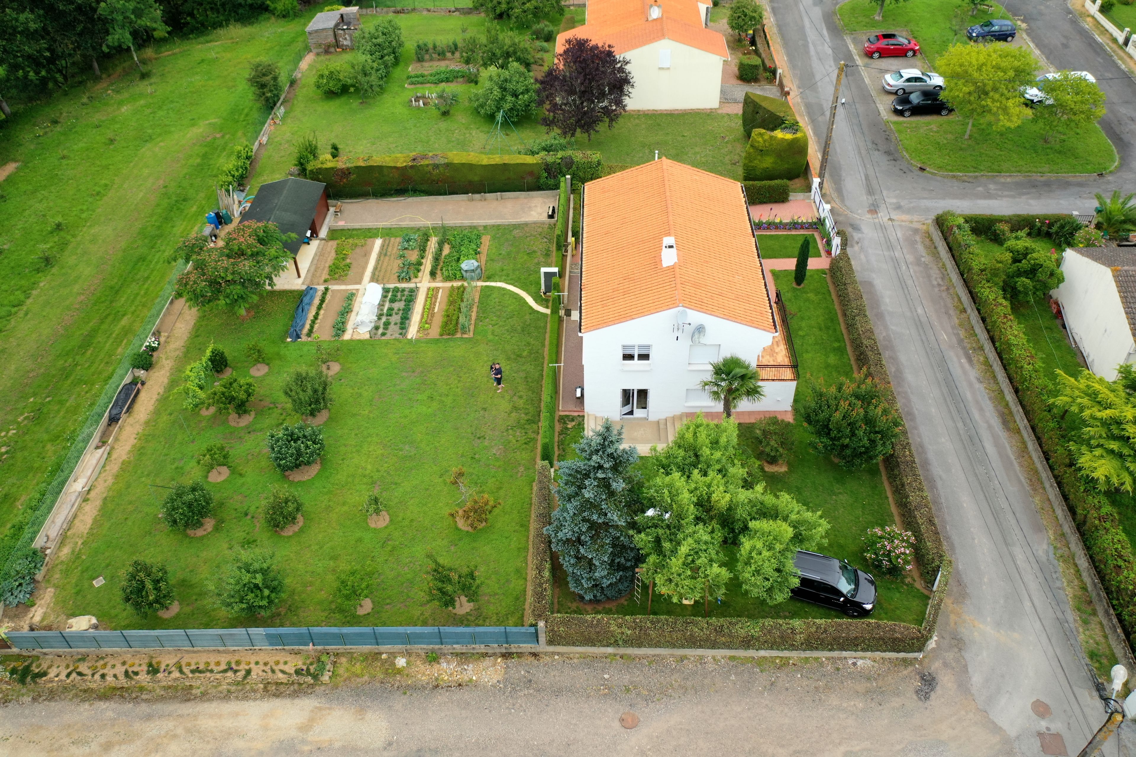 A residential property with a garden, a house with a red roof, and a driveway.