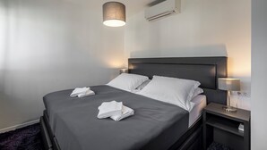 Una habitación de hotel moderna con cama, lámparas de noche, equipo de aire acondicionado y cabecera oscura.