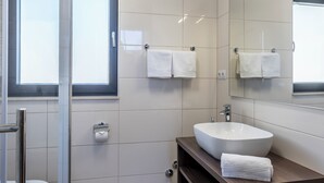 Un baño moderno con cabina de ducha de vidrio, un lavabo blanco y un espejo grande.