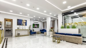 Un moderno vestíbulo de hotel con piso de mármol, sofás azules, una recepción y una pantalla grande.