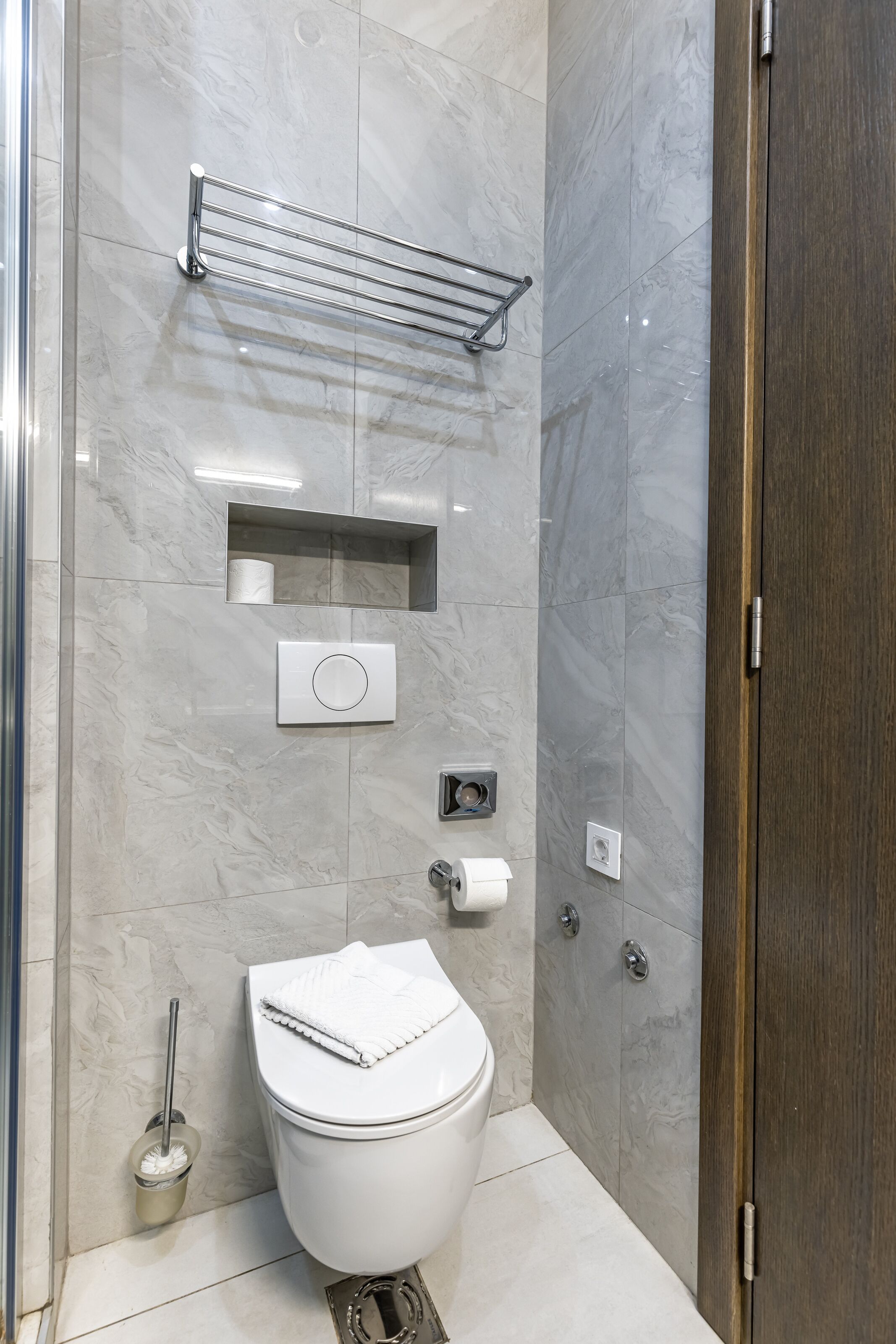 Un baño moderno con un inodoro, un secador de manos, un perchero para toallas y un dispensador de papel higiénico.