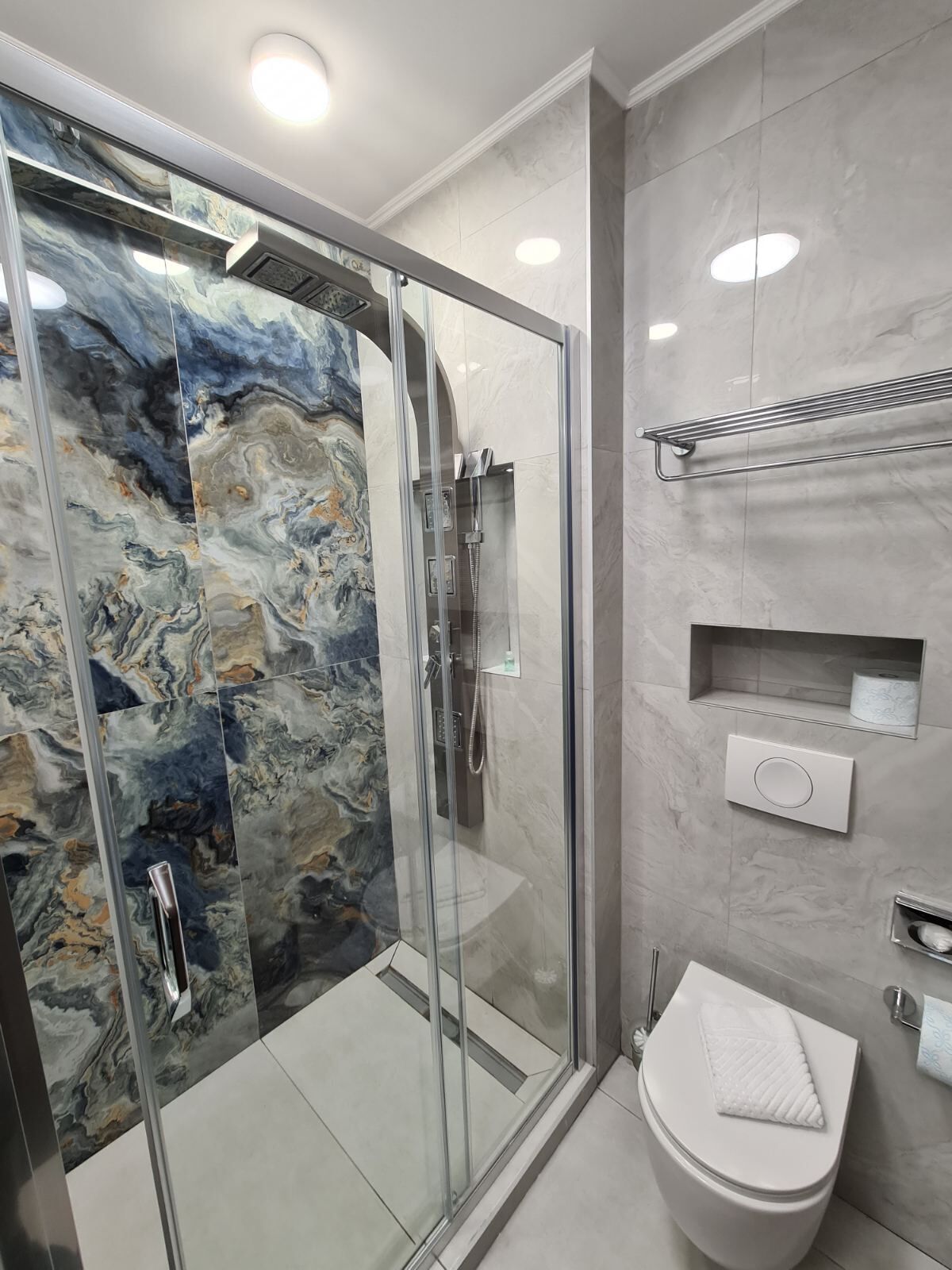 Une salle de bain moderne avec une douche en verre, des murs en marbre et des toilettes sur lesquelles est posée une serviette.