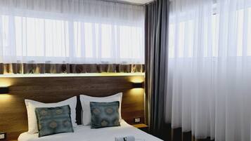 Une chambre d’hôtel avec un grand lit, une tête de lit en bois et une fenêtre ornée de rideaux légers.