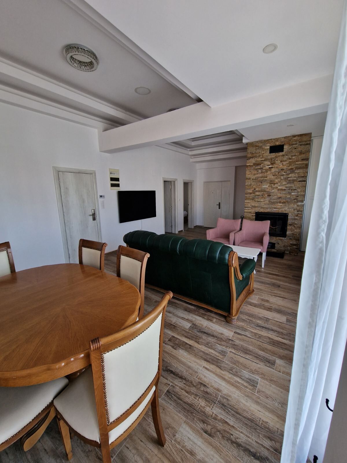 A spacious living area with a wooden dining table, a green sofa, and a pink armchair.
