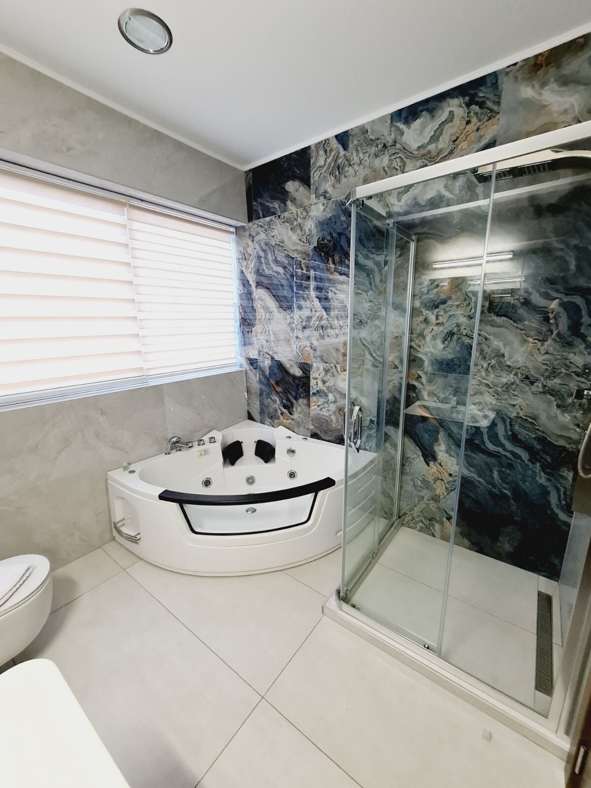 A modern bathroom with a marble wall, a glass shower enclosure, and a freestanding bathtub.