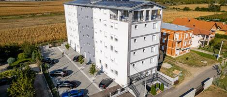 A multi-story building with solar panels on the roof, a parking lot, and a surrounding agricultural field.