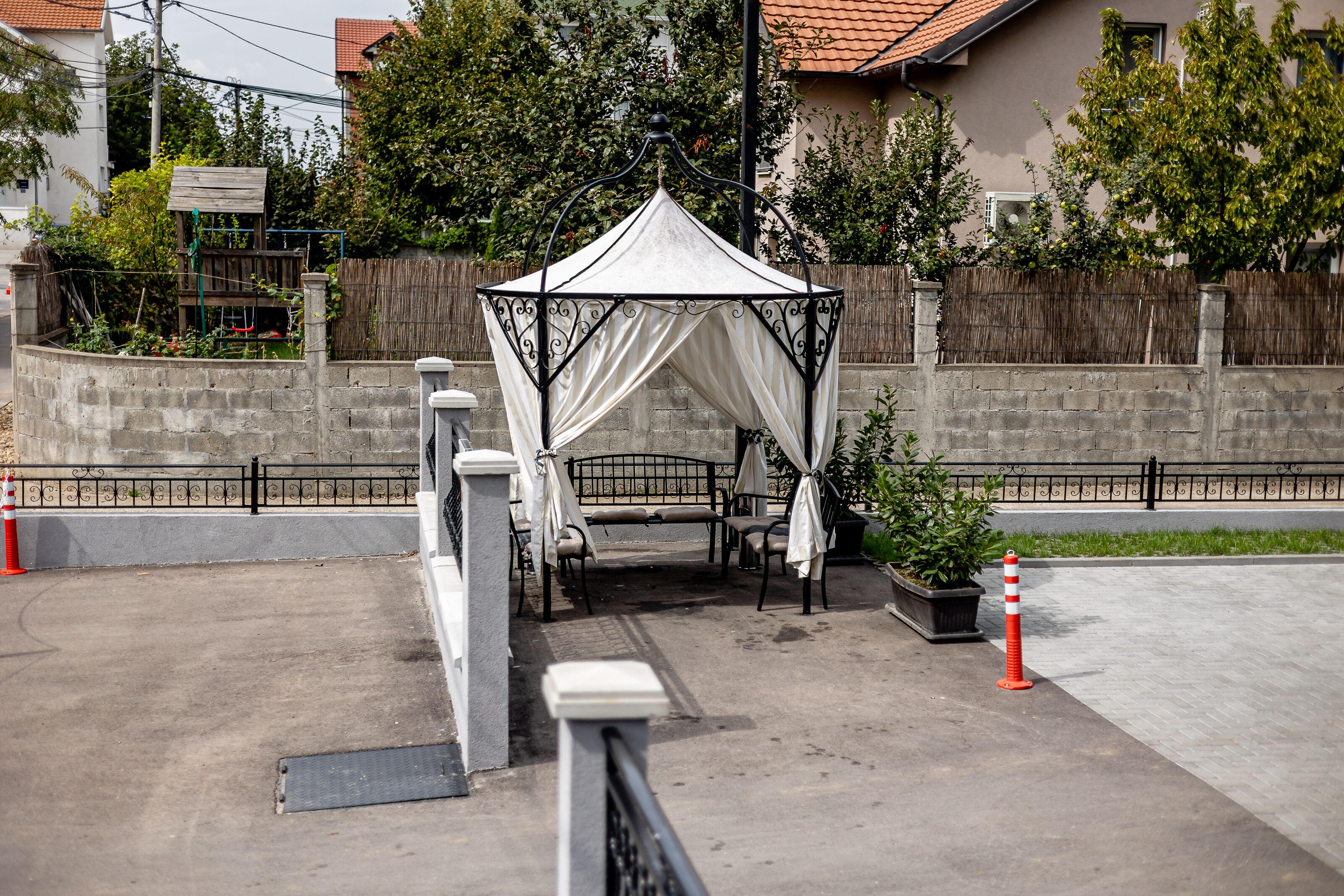 A gazebo with a white canopy and a bench, surrounded by a stone wall and a wooden fence.