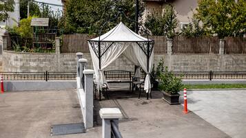 A gazebo with a white canopy and a bench, surrounded by a stone wall and a wooden fence.
