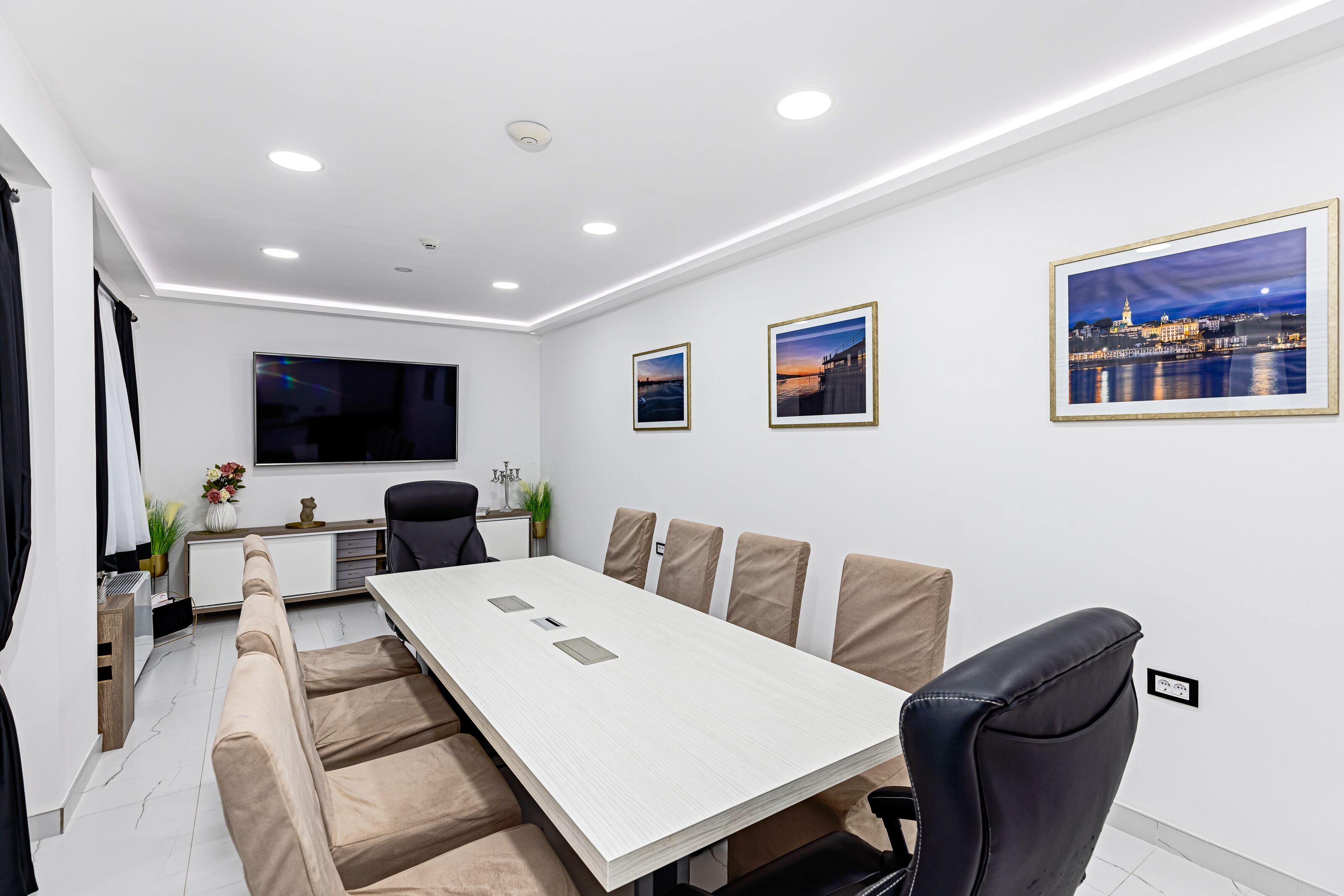 Una sala de reuniones moderna con una larga mesa, asientos cómodos, un televisor de pantalla plana y fotografías enmarcadas de la ciudad en las paredes.