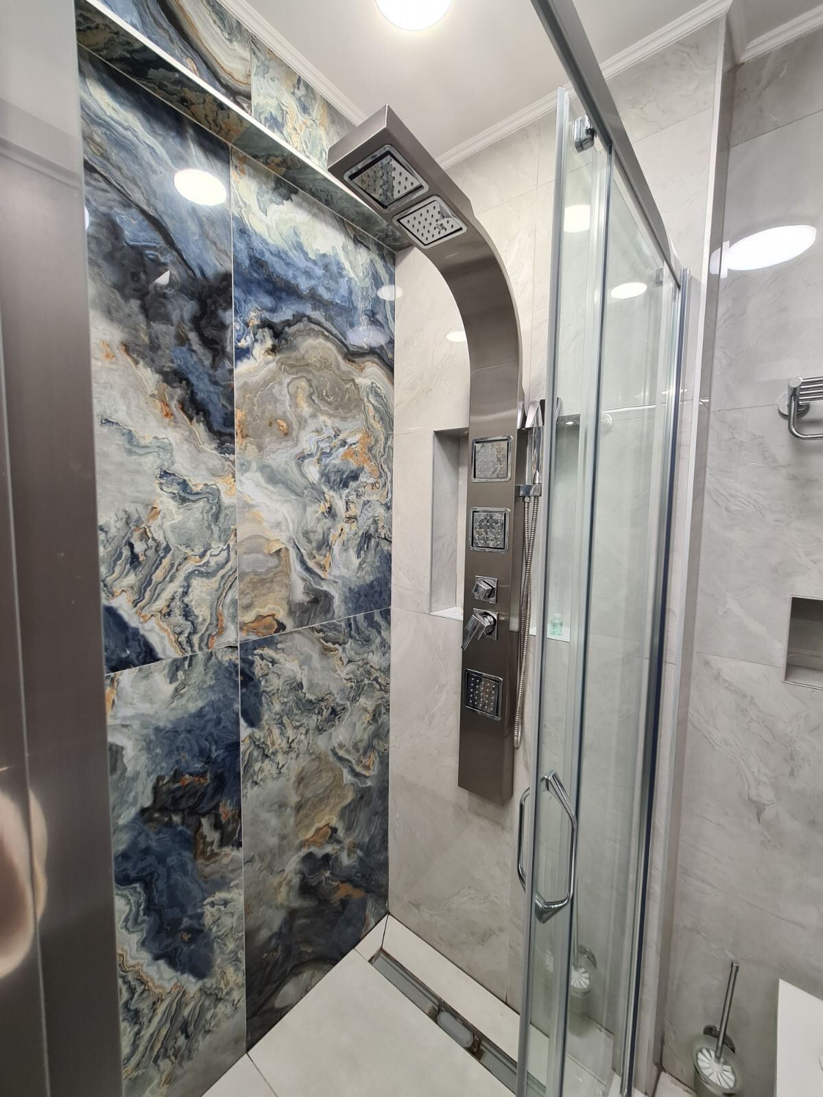 Une salle de bain moderne dotée d’une douche à parois de verre, de murs en marbre et d’un meuble-vasque intégré.