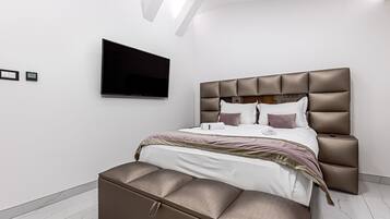 Une chambre à coucher moderne avec un grand lit, un téléviseur à écran plat fixé au mur et un banc intégré au pied du lit.