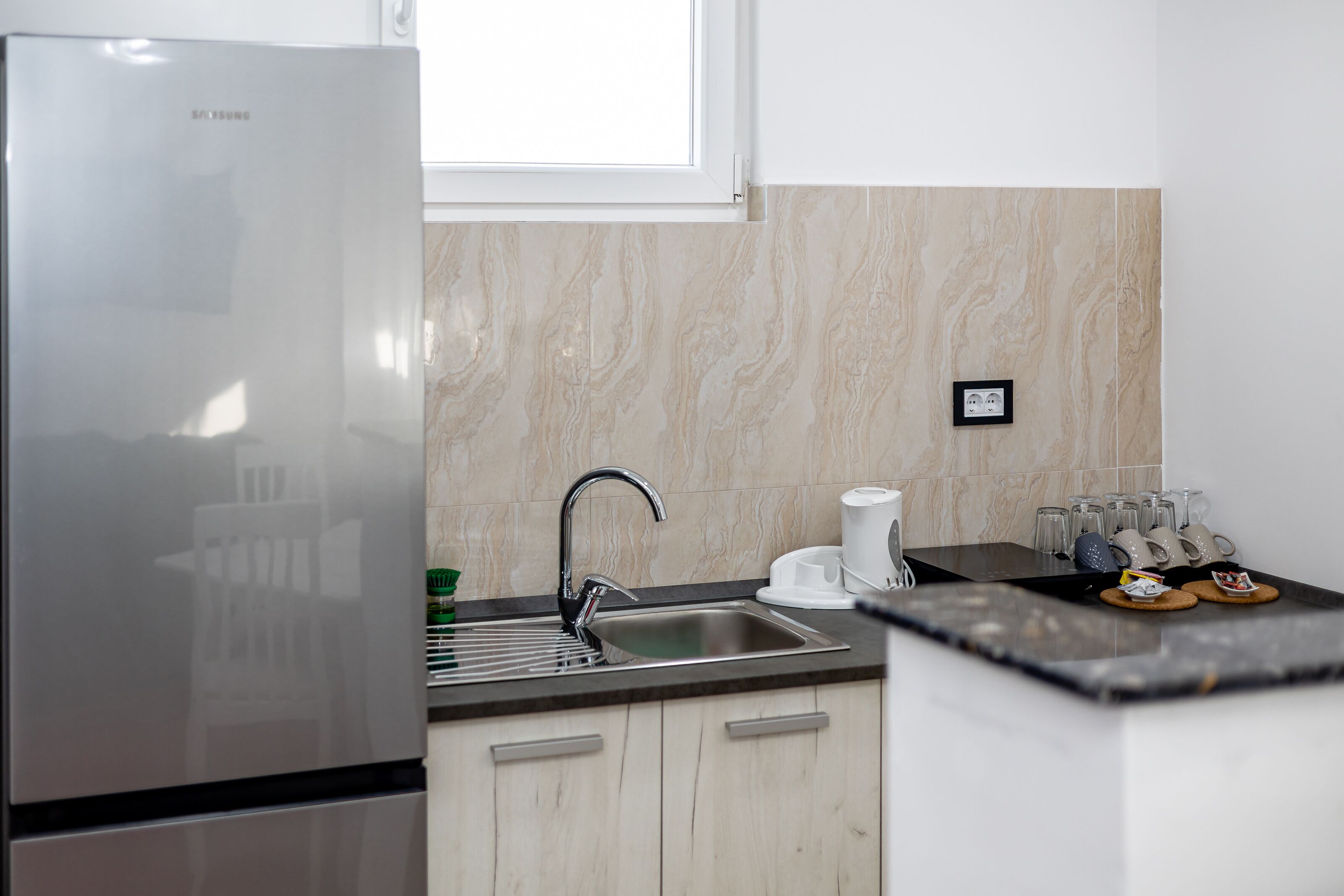 A modern kitchen with a stainless steel refrigerator, a sink, and a coffee maker.