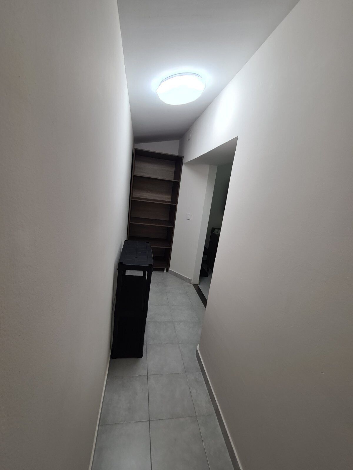 Ein schmaler, mit Fliesen ausgelegter Gang mit einem schwarzen Tisch und einer Treppe mit hölzernen Stufen.