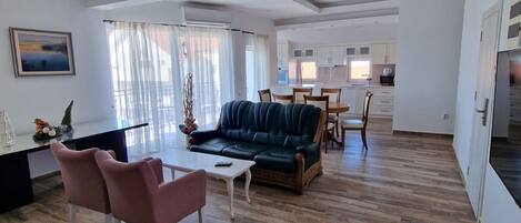 Amplia sala de estar con sofá, sillas y mesa de comedor. El piso es de madera y el techo tiene un diseño moderno.