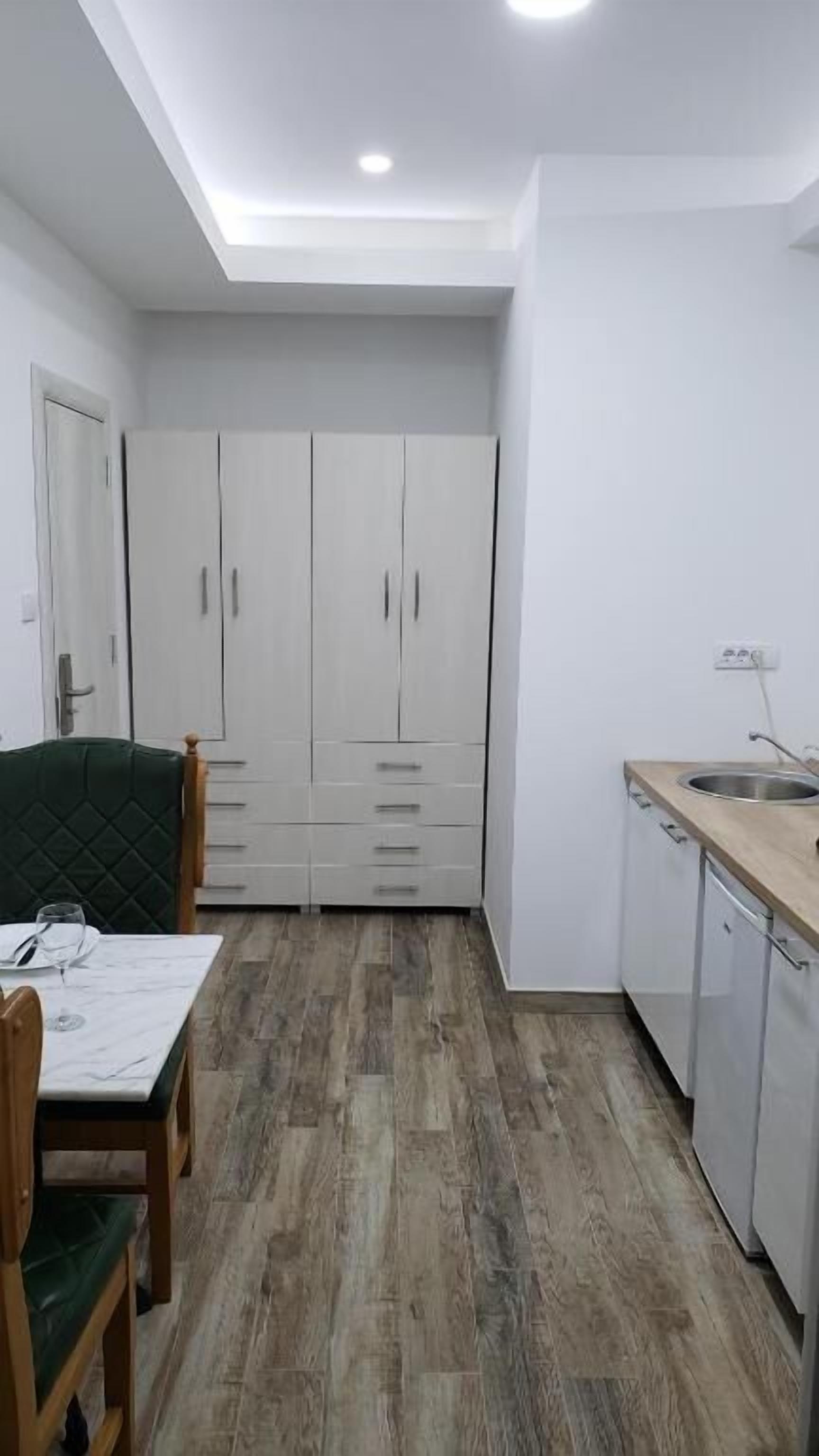 Cocina compacta con armarios blancos, encimera de madera y zona de comedor con mesa y sillas.