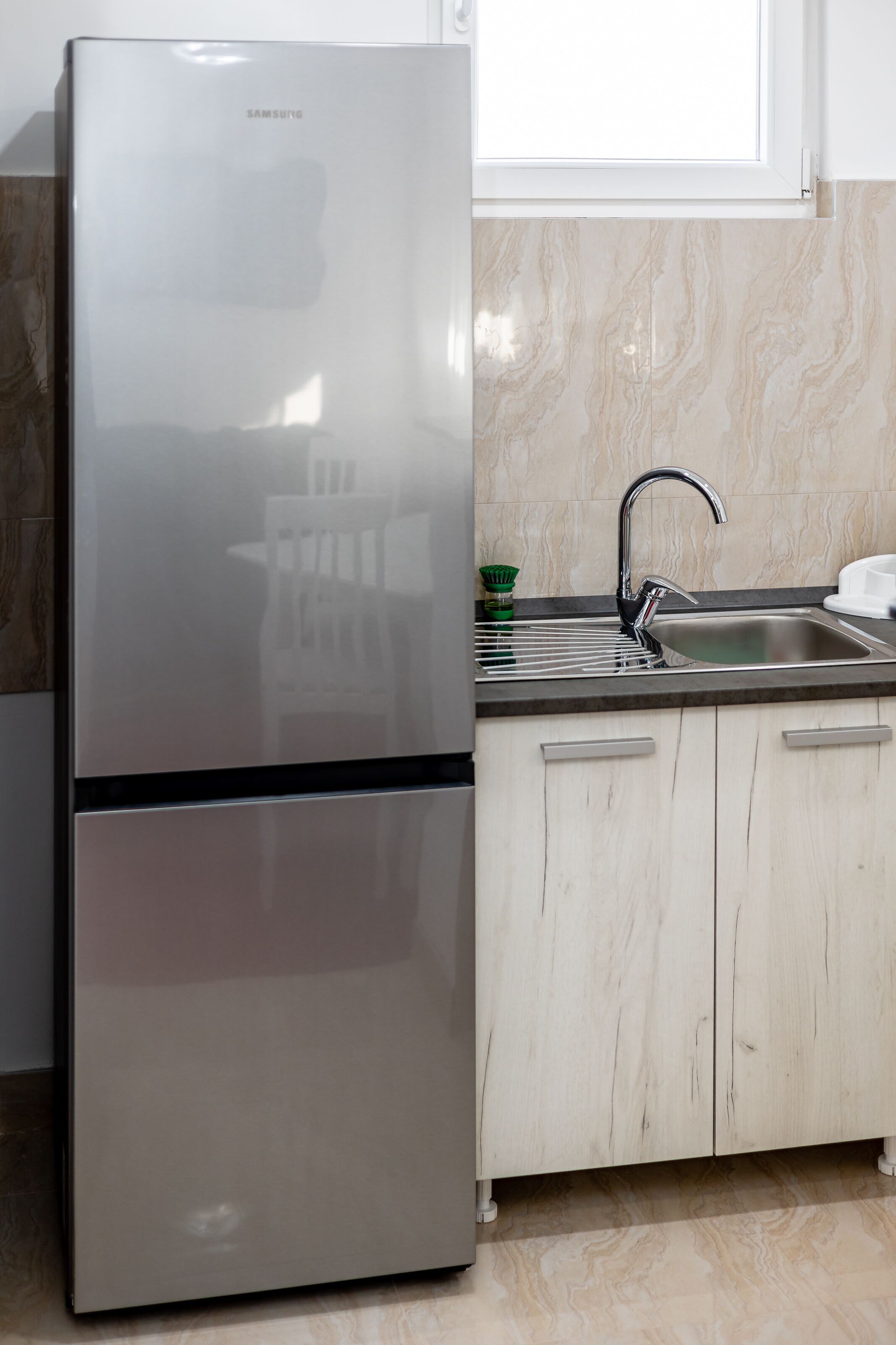 Una cocina con refrigerador de acero inoxidable, un lavamanos y armarios de tonos claros.