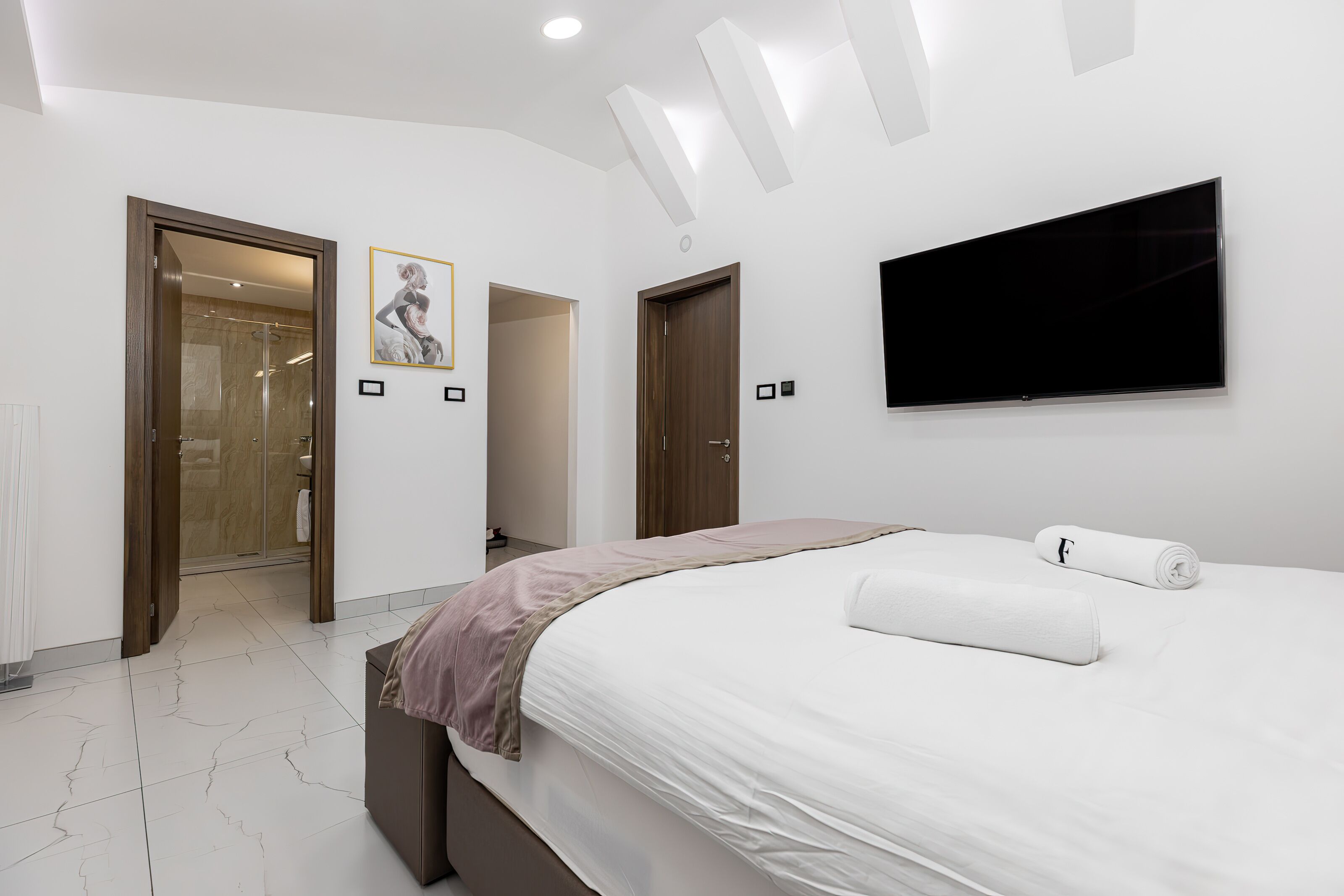 A modern bedroom with a large bed, a flat-screen TV, and two doors leading to other rooms.