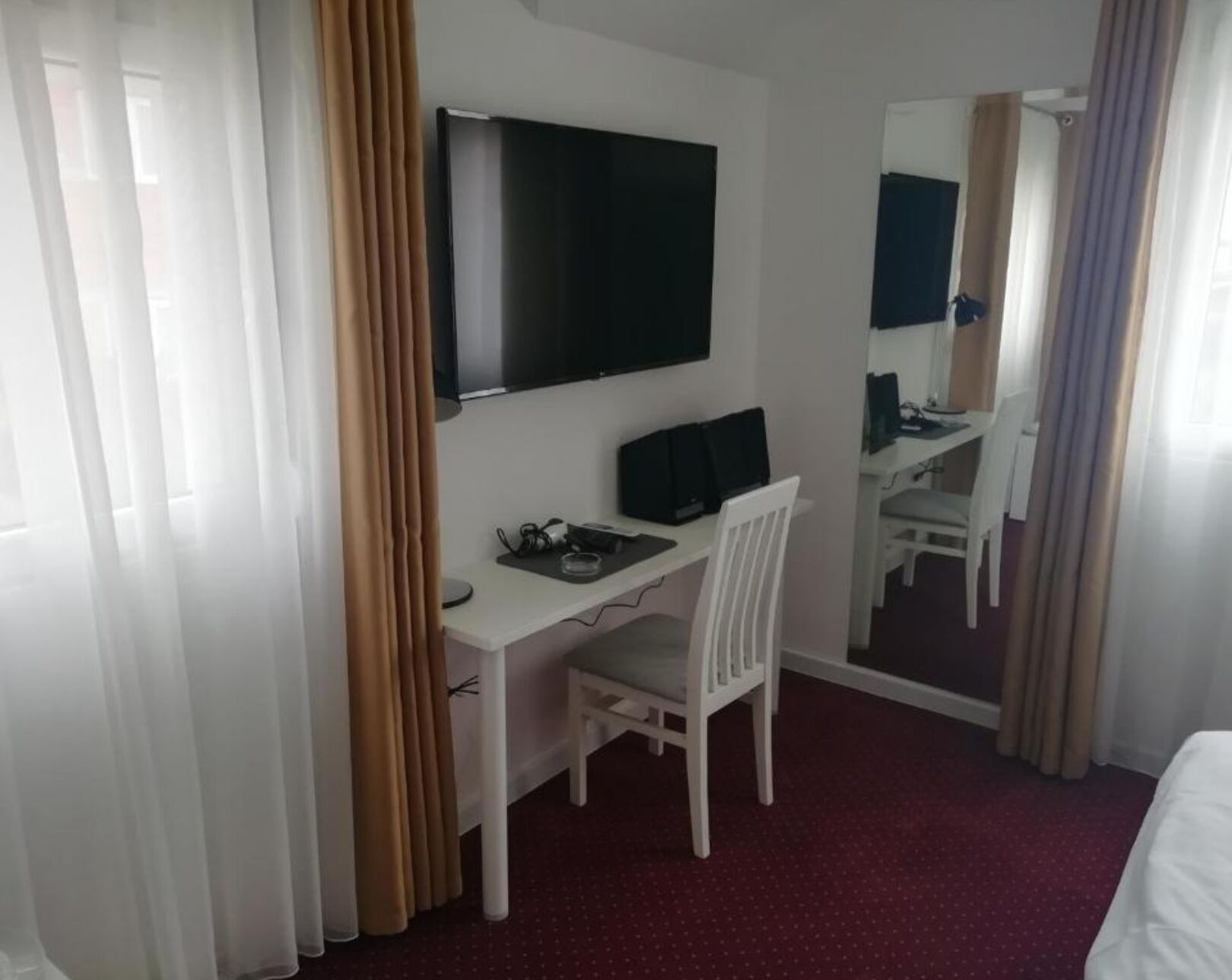 A hotel room with a desk, chair, TV, and a mirror.