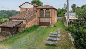 Una casa rústica con techo de tejas, una construcción anexa más pequeña y un jardín con una fila de tumbonas.