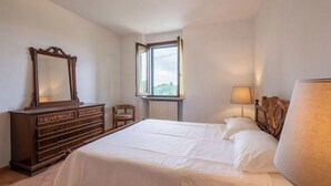 Un dormitorio con cama, cómoda, silla, ventana y lámpara.