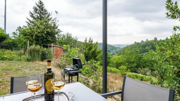 Una mesa con dos copas de vino y una botella, al aire libre, con una vista panorámica de colinas y vegetación.
