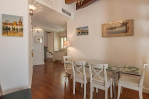 Un comedor con sillas blancas y una mesa de vidrio, una lámpara y cuadros en la pared.