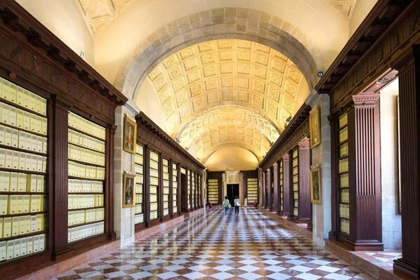 A long hallway with a checkered floor, bookshelves on both sides, and a high arched ceiling.