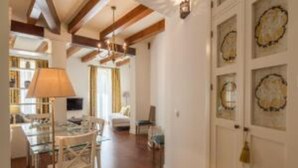 A room with wooden beams, a chandelier, a dining table with chairs, and a wall with framed pictures. - Roof Cathedral Sevilla (Sevilla)